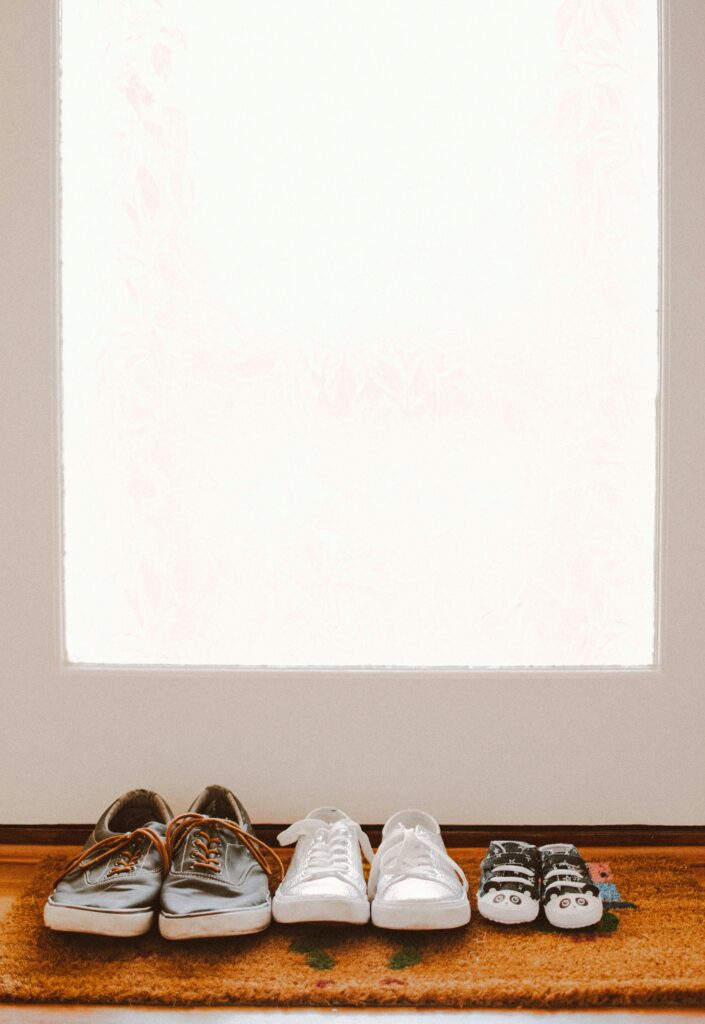 A collection of family shoes, including baby booties, on a welcoming mat by the door.